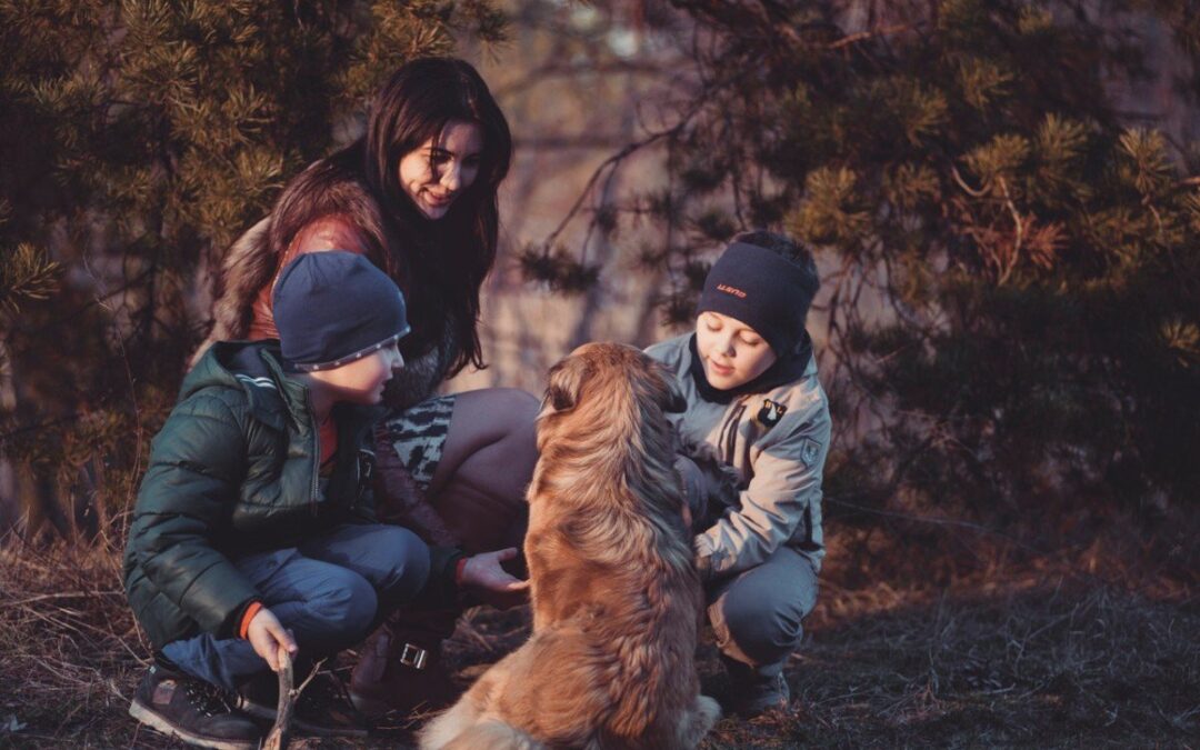 three people crouching in front of a sitting dog