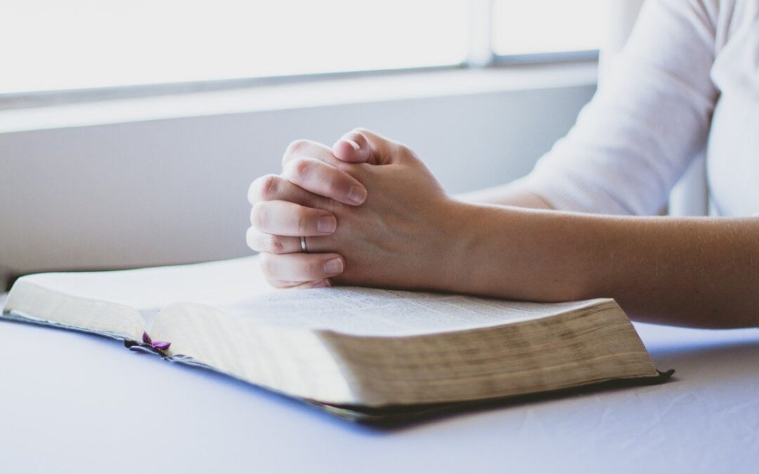 woman praying with both hands on top of the bible
